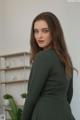 A woman in a green dress standing in front of a shelf.