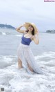 A woman in a blue top and a white skirt standing in the ocean.