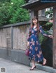 A woman in a blue floral dress standing in front of a building.