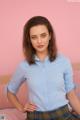 A woman in a blue shirt and plaid skirt posing on a bed.